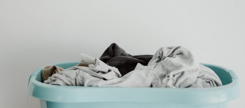 A green mint-blue laundry basket full of unwashed clothes