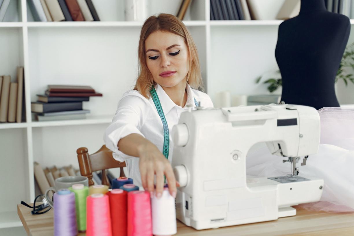 Dressmaker touching white-colored thread placed beside her sewing machine