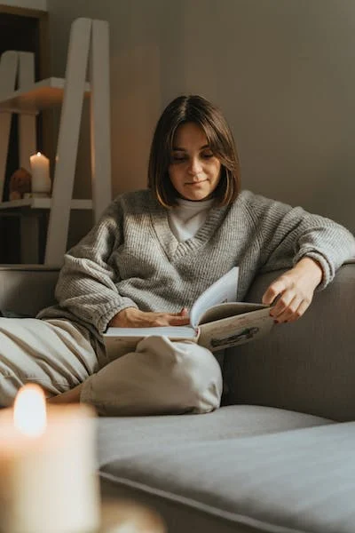 A woman sitting on a couch in her sweater and reading
