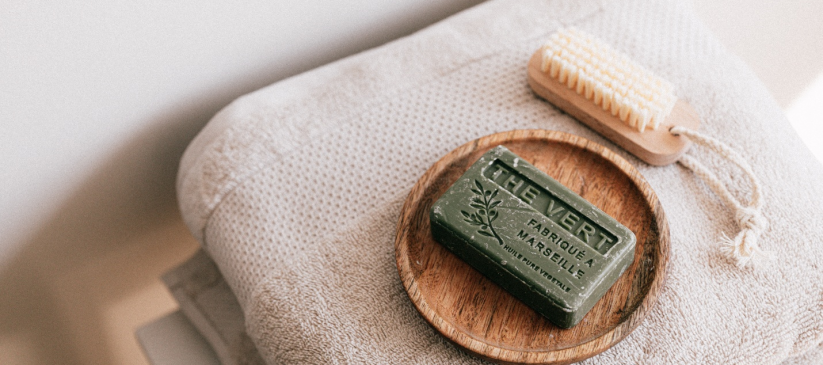 A bar of green organic soap and a brush are placed on top of white towels.