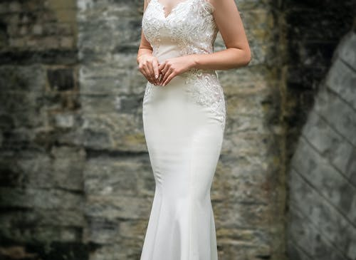 A woman in a white wedding dress standing near a brick wall