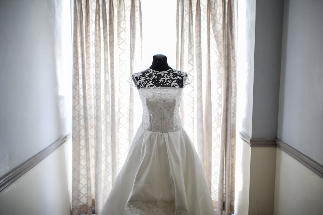 A clean wedding dress on display in front of a window with curtains