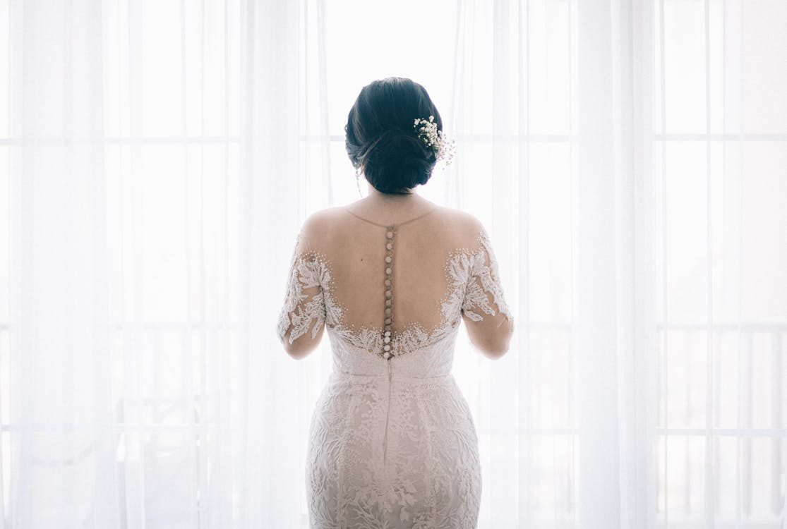 A woman wearing a white lace wedding dress near a white curtain