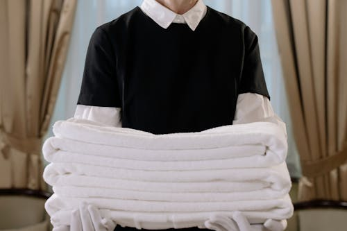 A hotel employee in a clean uniform holding a stack of towels